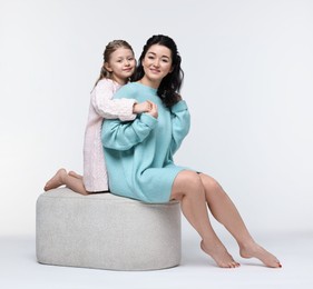 Photo of Beautiful mother hugging with little daughter on pouf against white background