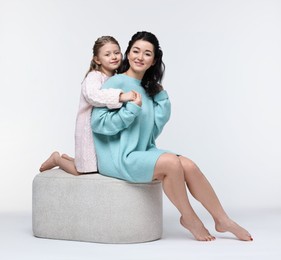 Beautiful mother hugging with little daughter on pouf against white background