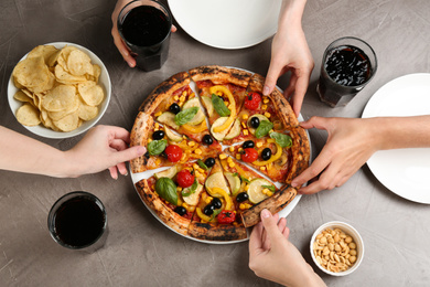 Women taking slices of delicious vegetable pizza at grey table, closeup