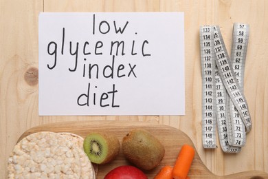 Photo of Paper with words Low Glycemic Index Diet, measuring tape and healthy products on wooden table, flat lay