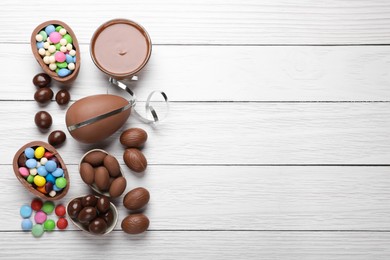 Photo of Delicious chocolate eggs, paste and candies on white wooden table, flat lay. Space for text