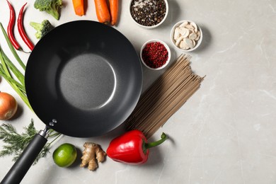 Photo of Empty iron wok surrounded by raw ingredients on light table, flat lay. Space for text