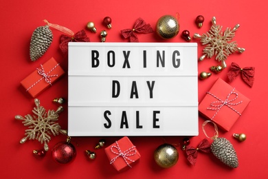 Photo of Lightbox with phrase BOXING DAY SALE and Christmas decorations on red background, flat lay