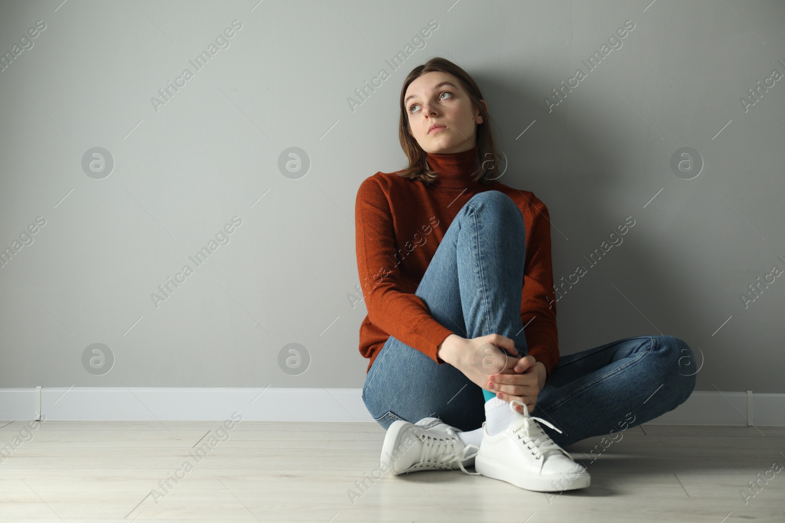 Photo of Sad young woman sitting on floor near grey wall indoors, space for text