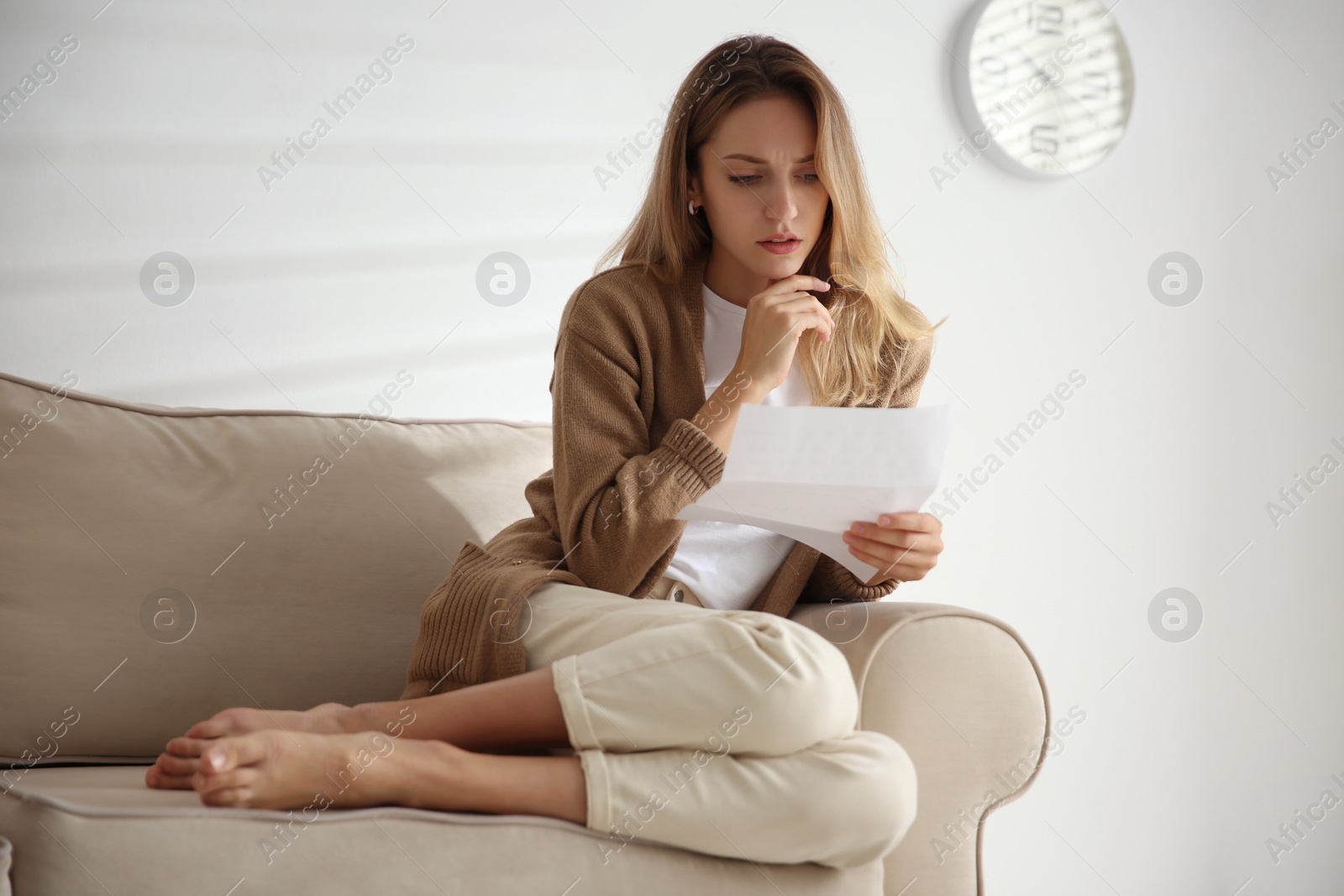 Photo of Worried woman reading letter on sofa at home