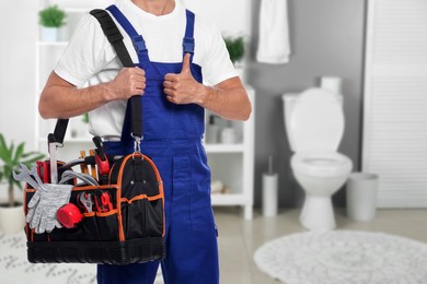Image of Plumber with bag of instruments showing thumbs up in bathroom, closeup. Space for text