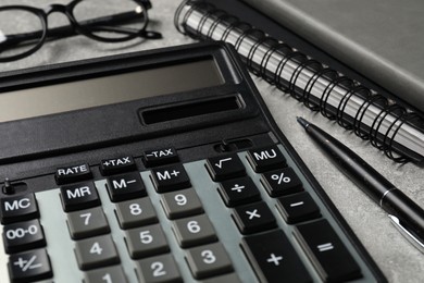 Calculator and office stationery on grey table, closeup