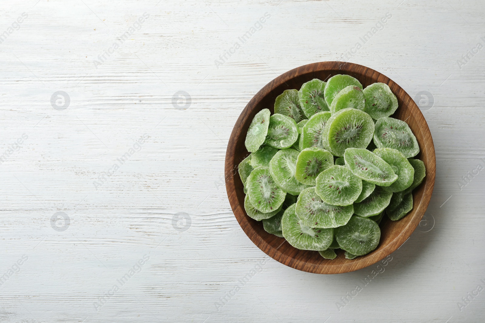 Photo of Bowl of dried kiwi on wooden background, top view with space for text. Tasty and healthy fruit