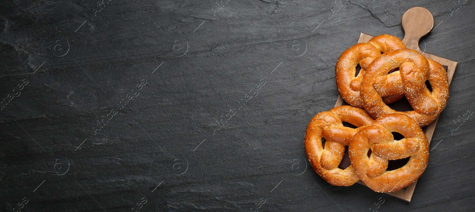 Image of Delicious pretzels with sesame seeds on black table, top view with space for text. Banner design