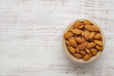 Photo of Tasty almonds in bowl on white wooden table, top view. Space for text