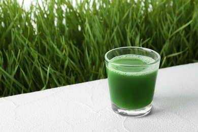 Photo of Glass of juice and fresh wheat grass on background. Space for text