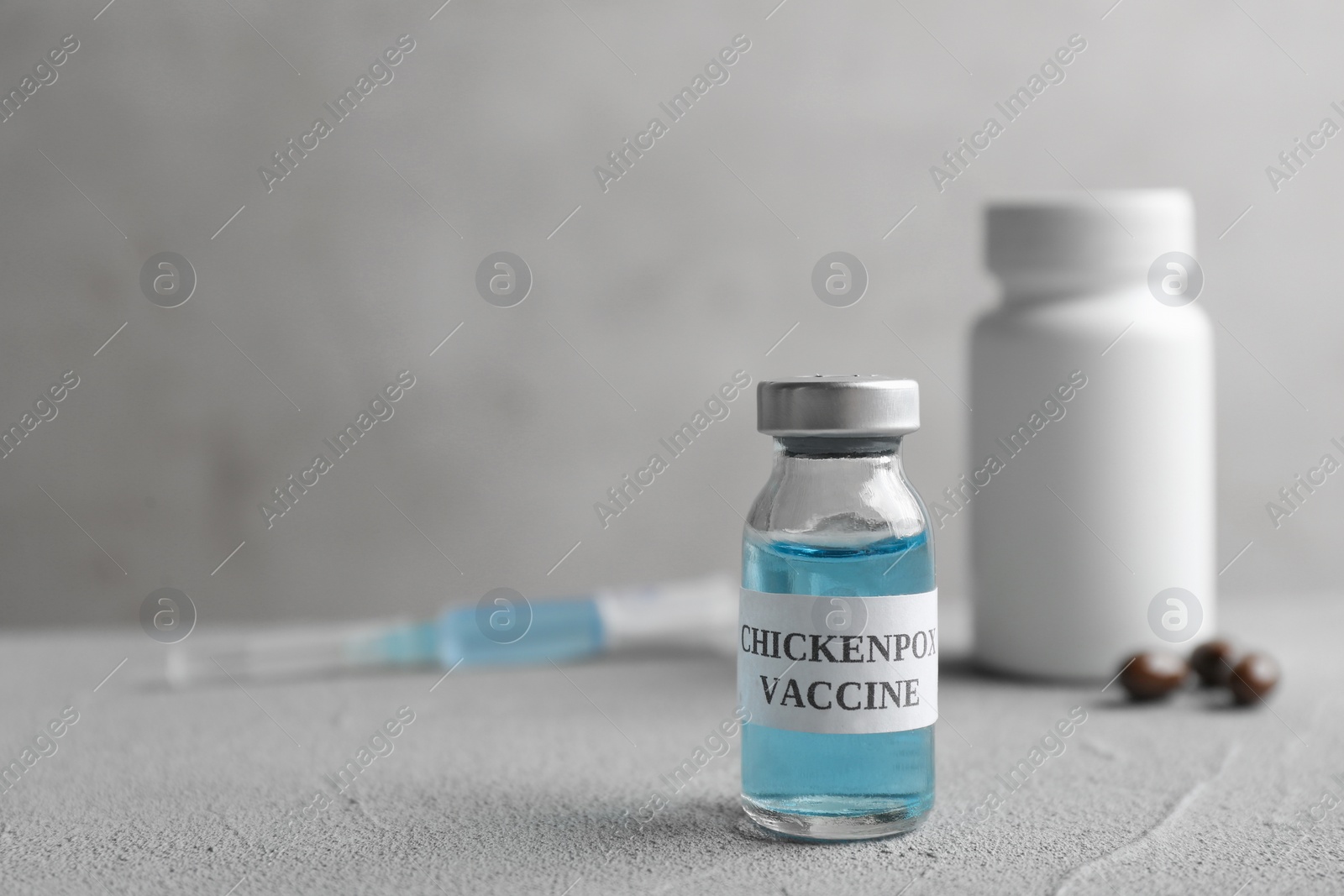 Photo of Chickenpox vaccine and syringe on grey table, space for text. Varicella virus prevention