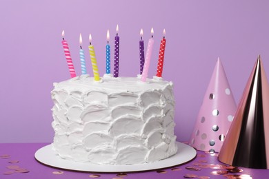 Photo of Delicious cake with burning candles and festive decor on purple background