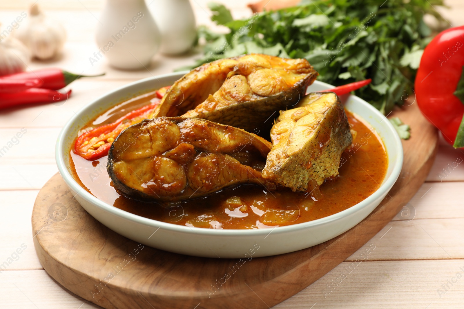 Photo of Tasty fish curry and ingredients on white wooden table, closeup. Indian cuisine