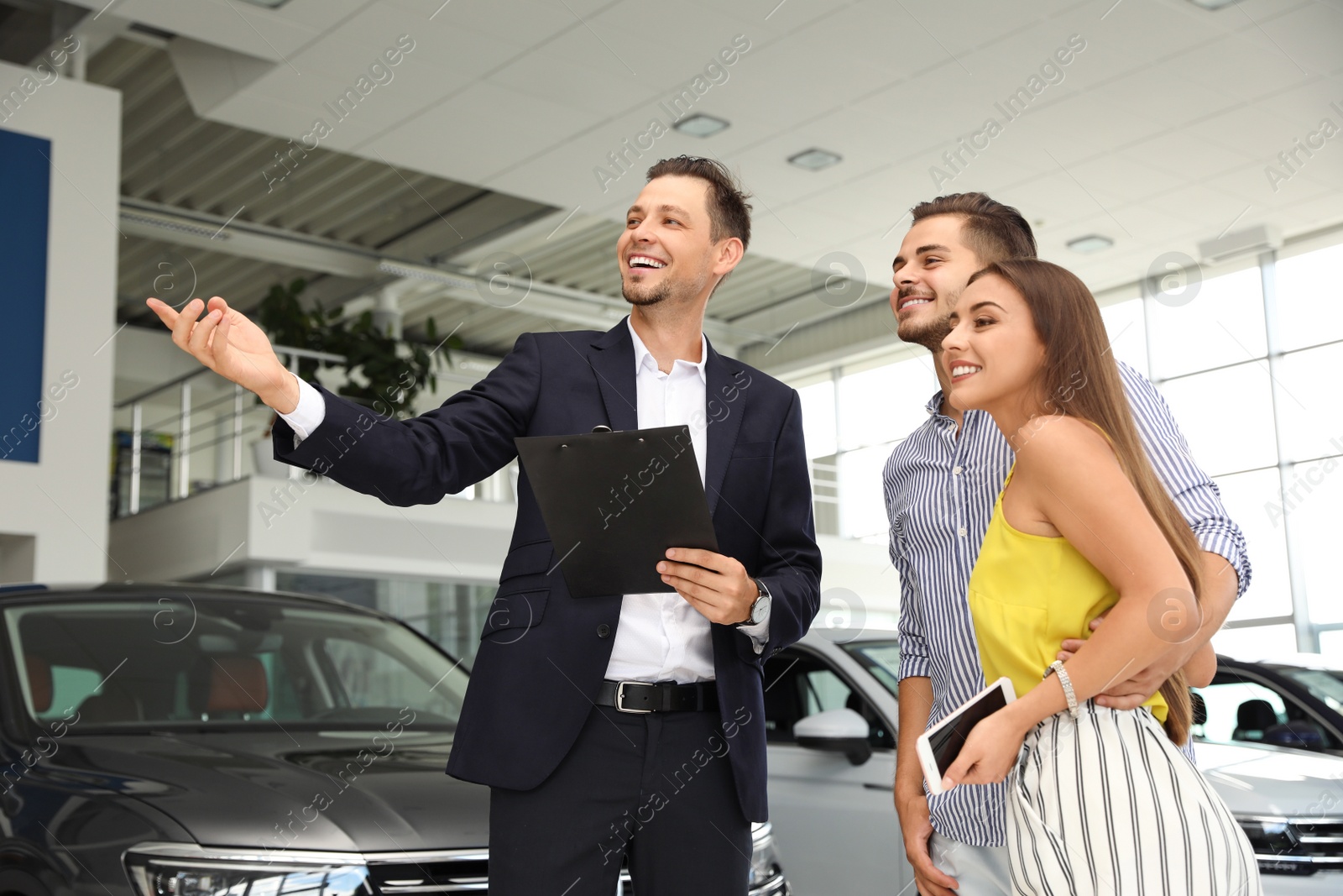 Photo of Young couple choosing new car with salesman in salon