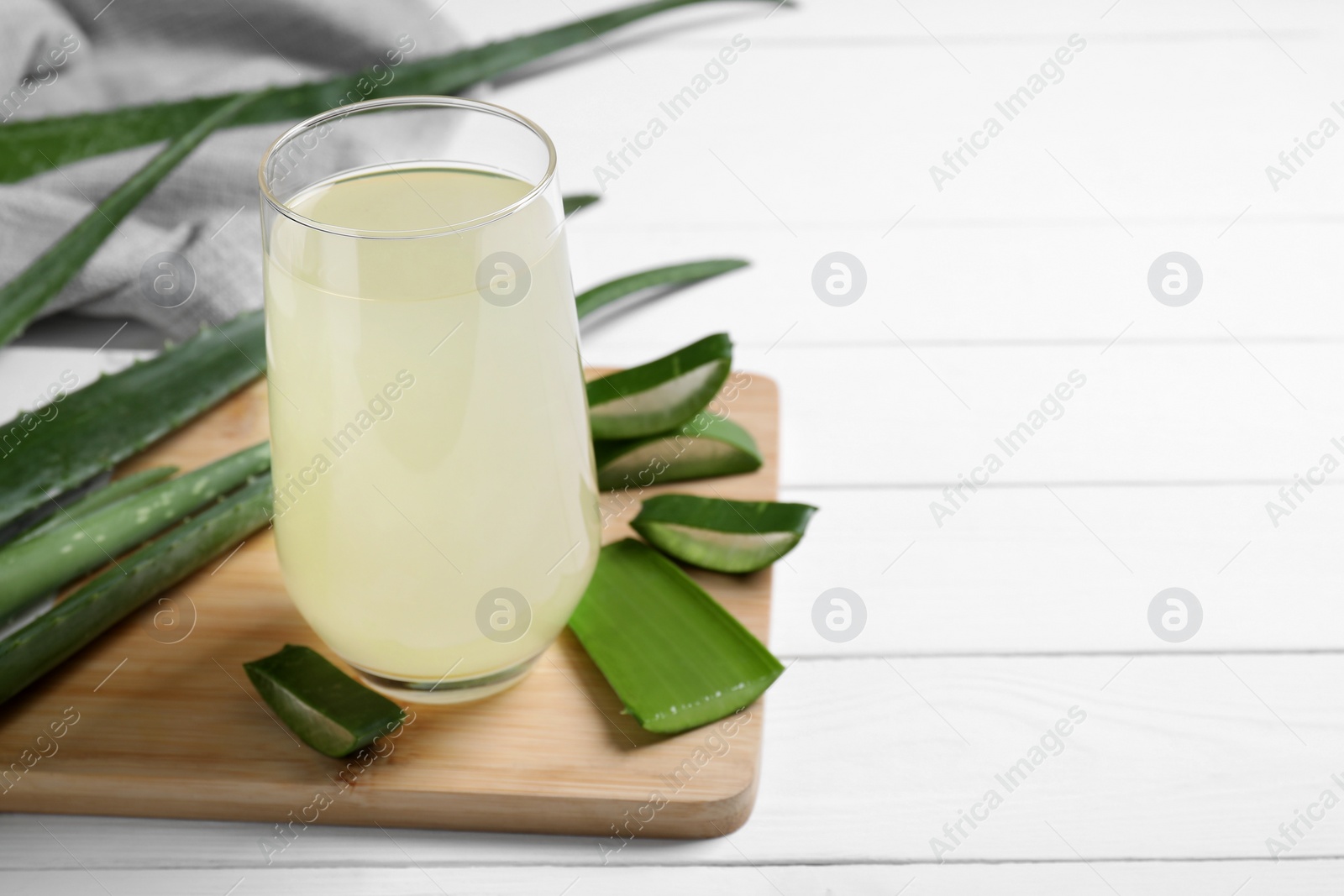 Photo of Fresh aloe juice in glass and leaves on white wooden table, closeup. Space for text