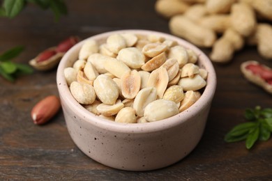 Fresh peeled peanuts in bowl on wooden table, closeup