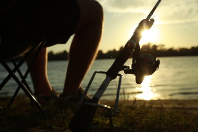 Photo of Fisherman with rod sitting on folding chair and fishing at riverside, closeup