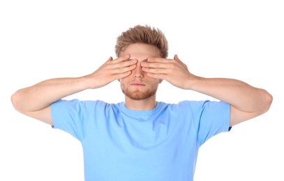Young man being blinded and covering eyes with hands on white background