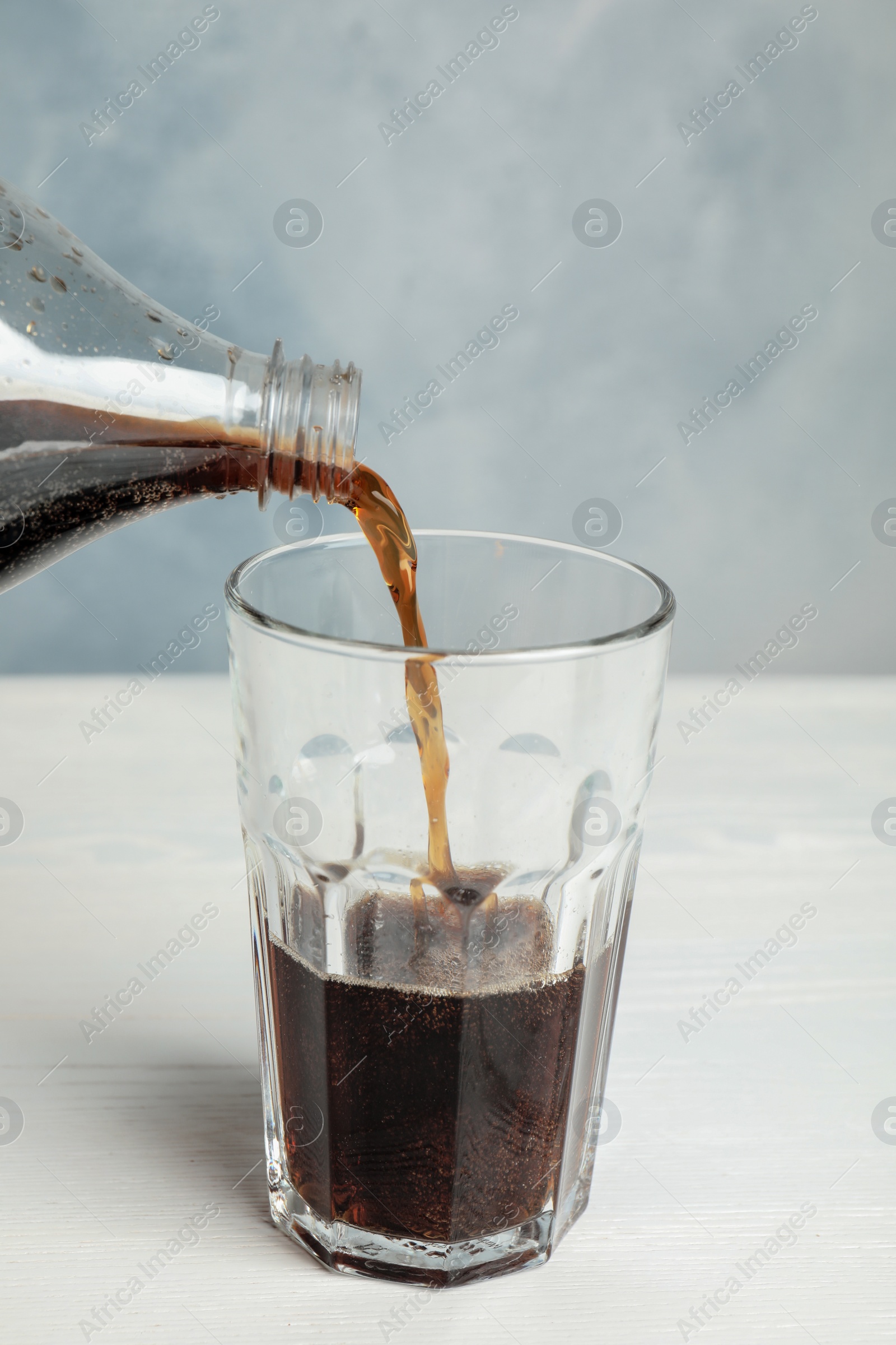 Photo of Pouring refreshing soda drink into glass on white wooden table against blue background