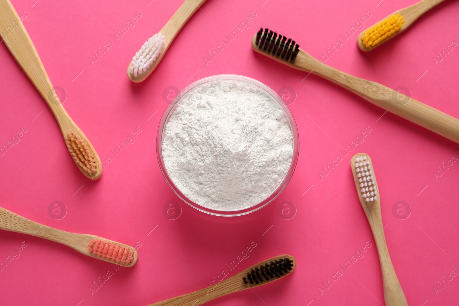Photo of Bowl of tooth powder and brushes on pink background, flat lay