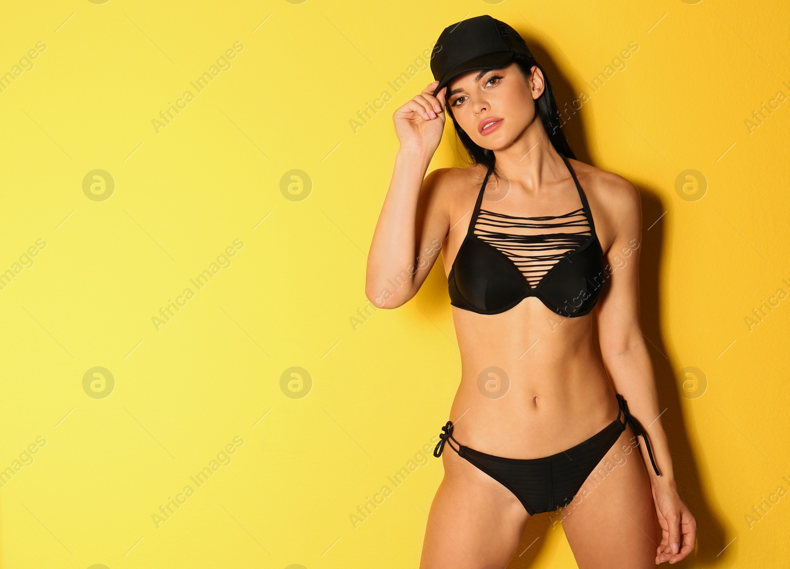 Photo of Beautiful young woman in black bikini on yellow background. Space for text