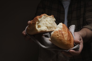 Man breaking loaf of fresh bread on dark background, closeup