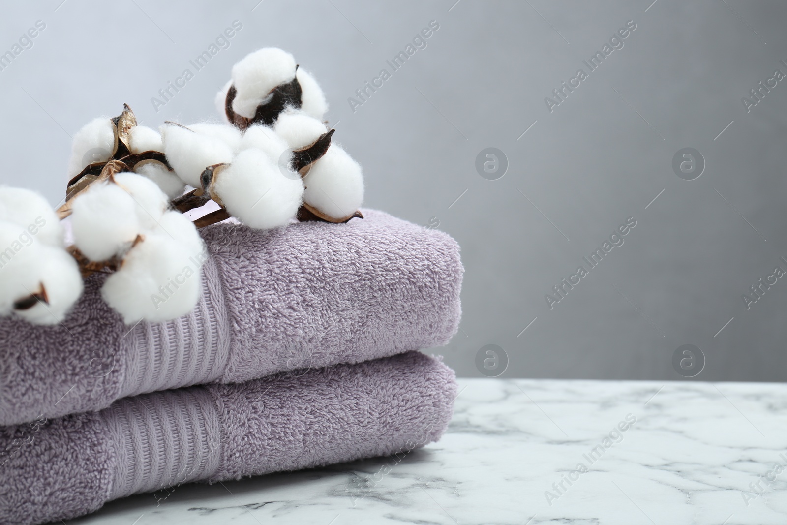 Photo of Violet terry towels and cotton flowers on white marble table, closeup. Space for text