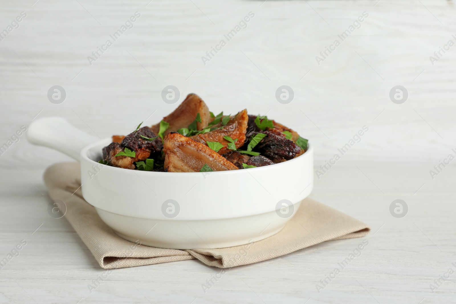 Photo of Tasty fried cracklings with parsley on white wooden table. Cooked pork lard