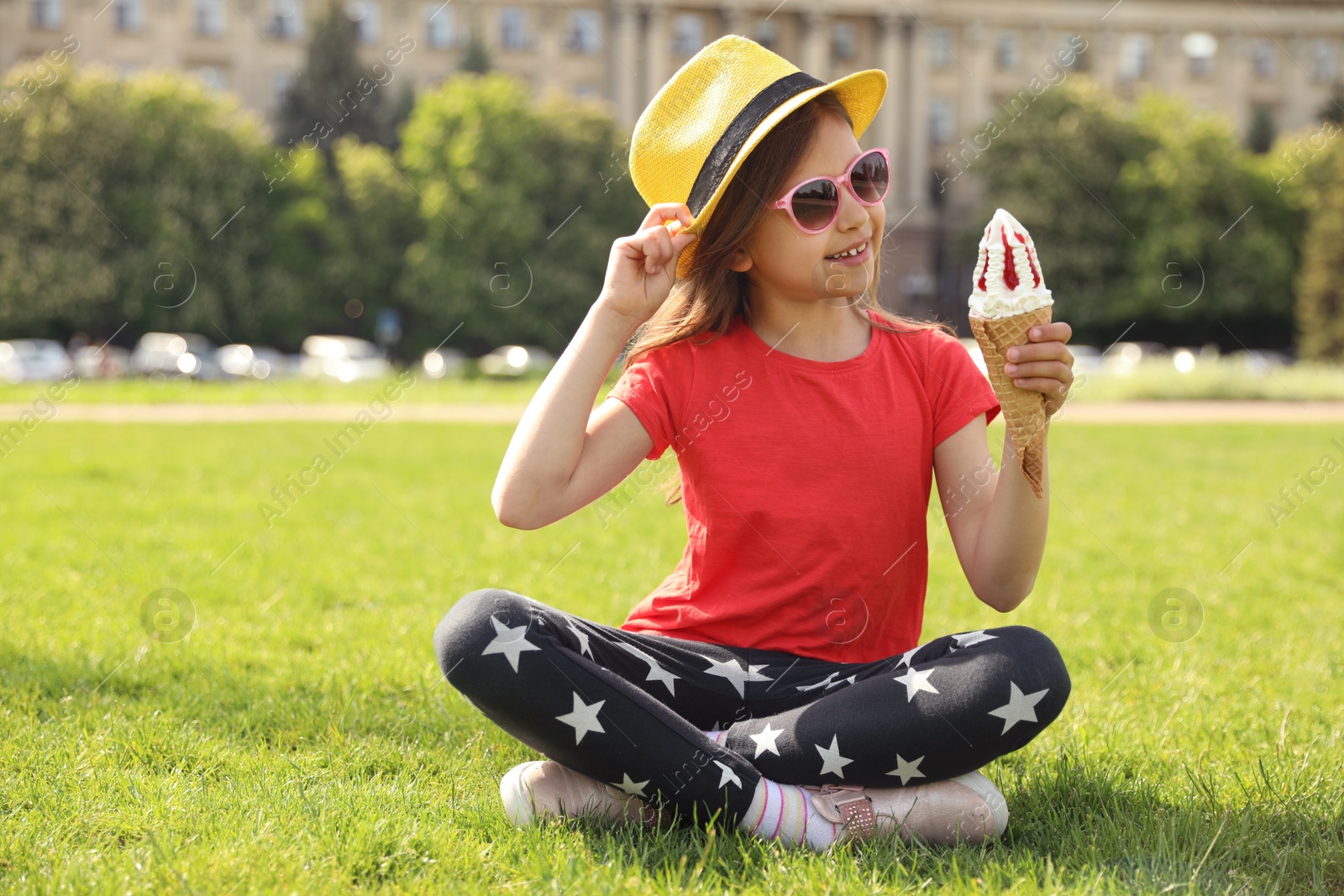 Photo of Cute little girl with delicious ice cream sitting on green grass outdoors