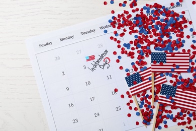 Photo of Flat lay composition with calendar, USA flags and colorful confetti on wooden background. Happy Independence Day