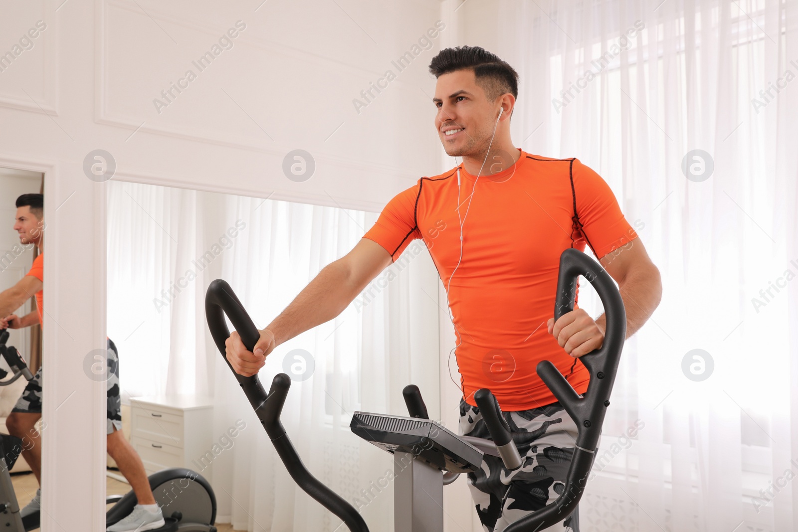 Photo of Man using modern elliptical machine at home