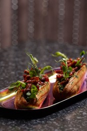 Photo of Tasty eclairs with sun-dried tomatoes and microgreens on dark table