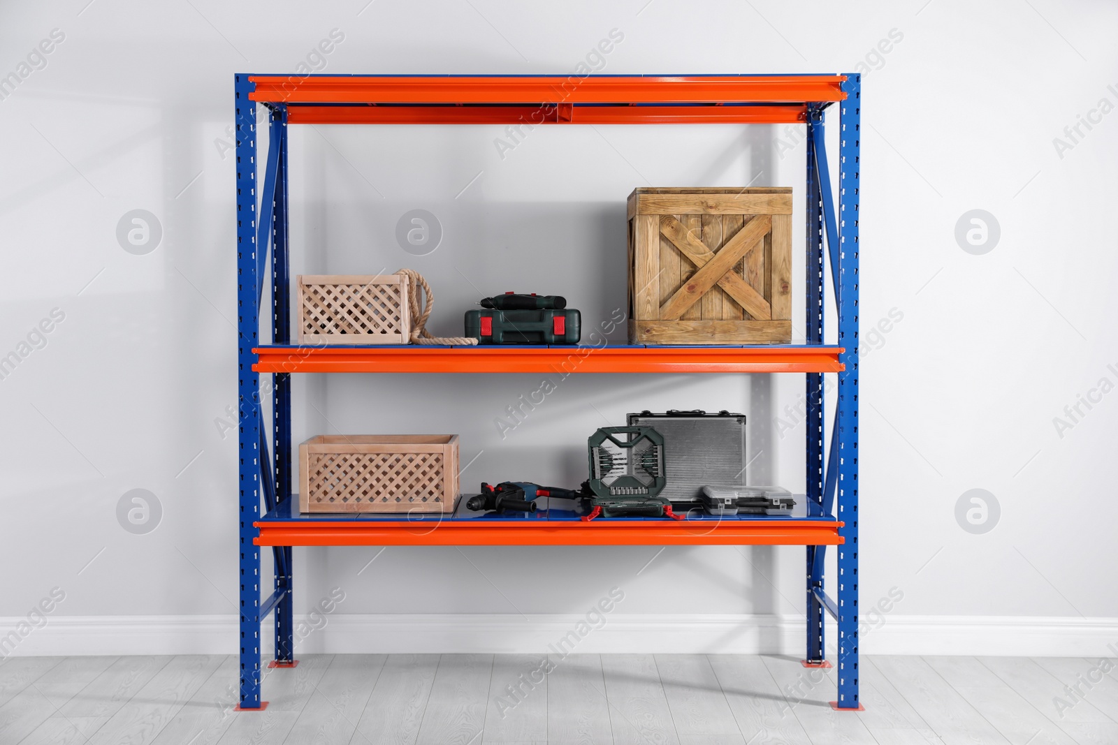 Photo of Metal shelving unit with wooden crates and different instruments near light wall indoors