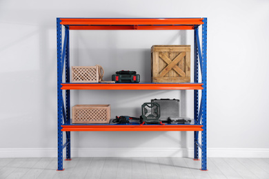 Photo of Metal shelving unit with wooden crates and different instruments near light wall indoors