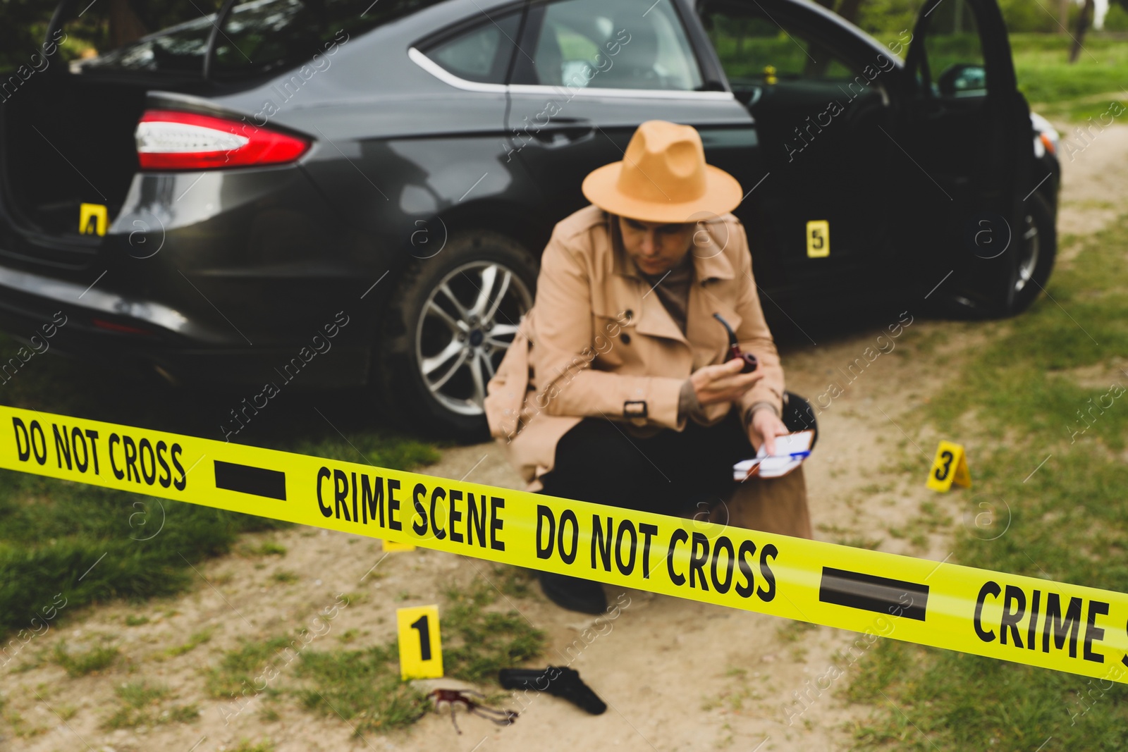 Photo of Professional detective examining crime scene outdoors, focus on yellow tape