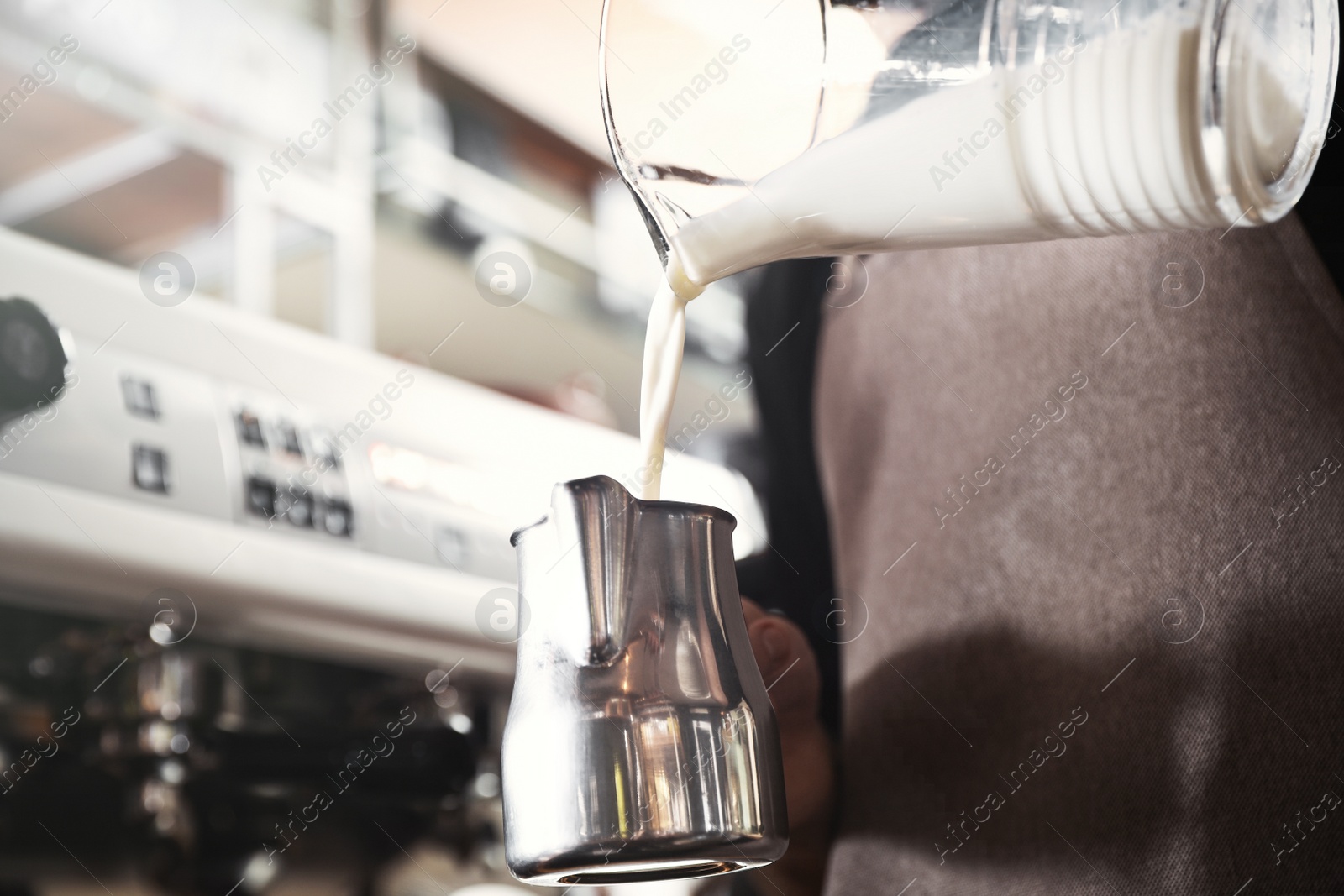 Photo of Barista pouring milk into metal pitcher indoors, closeup with space for text. Coffee making