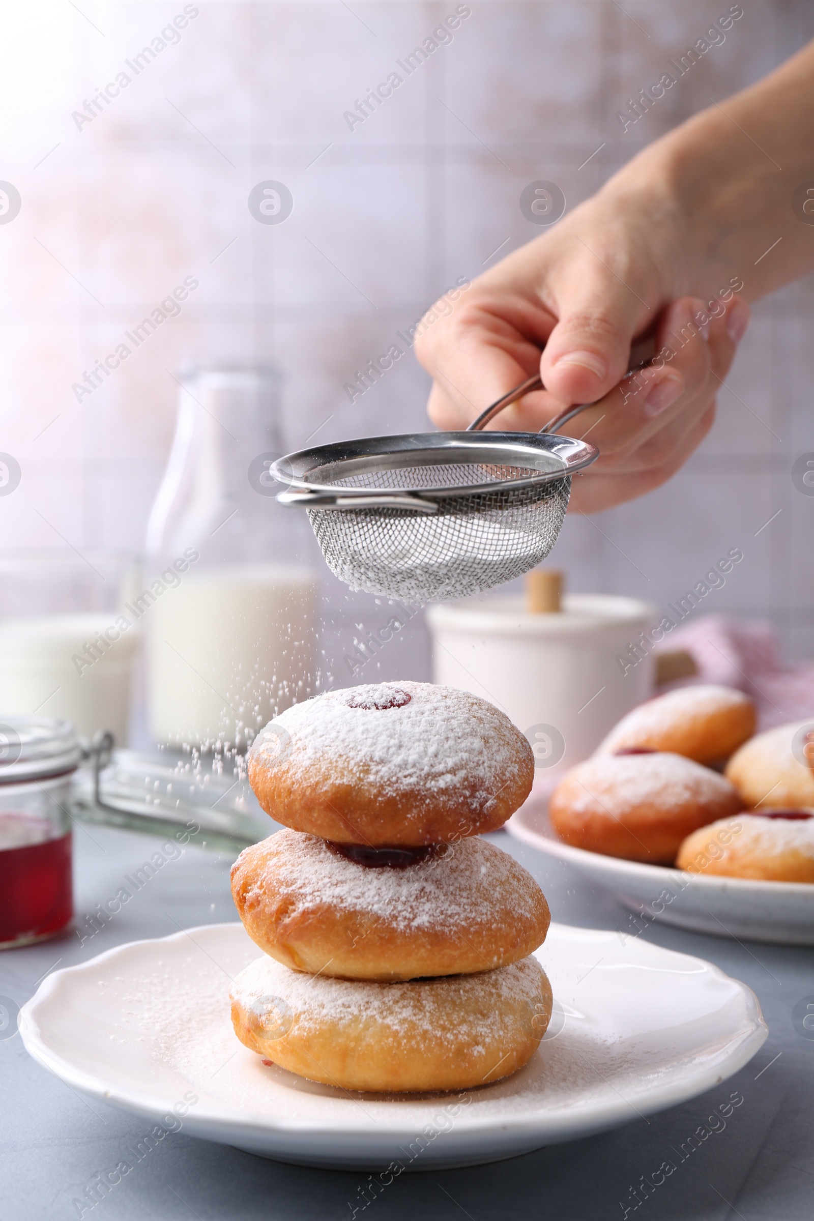 Photo of Woman dusting powdered sugar onto delicious Hanukkah donuts on light grey table, closeup