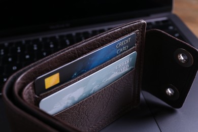 Photo of Credit cards in leather card holder and laptop on table, closeup