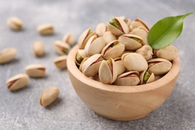 Delicious pistachios in bowl on grey textured table