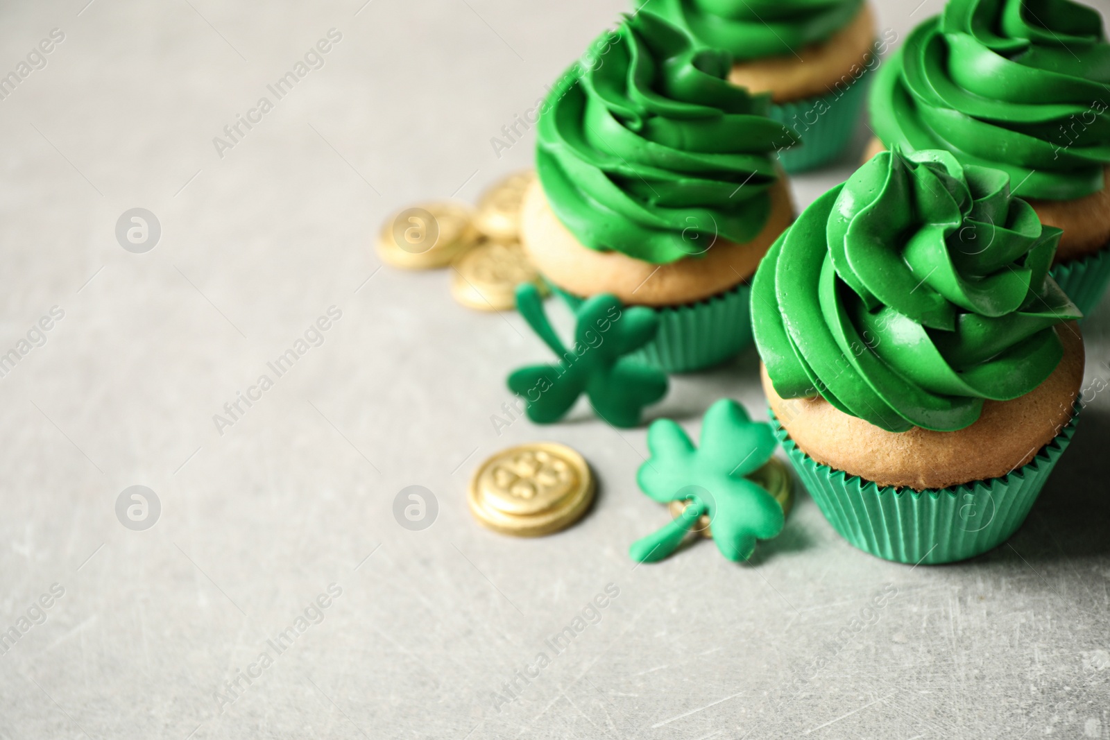 Photo of Decorated cupcakes and coins on grey table, space for text. St. Patrick's Day celebration