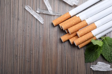 Photo of Cigarettes, menthol crystals and mint on wooden table, flat lay. Space for text
