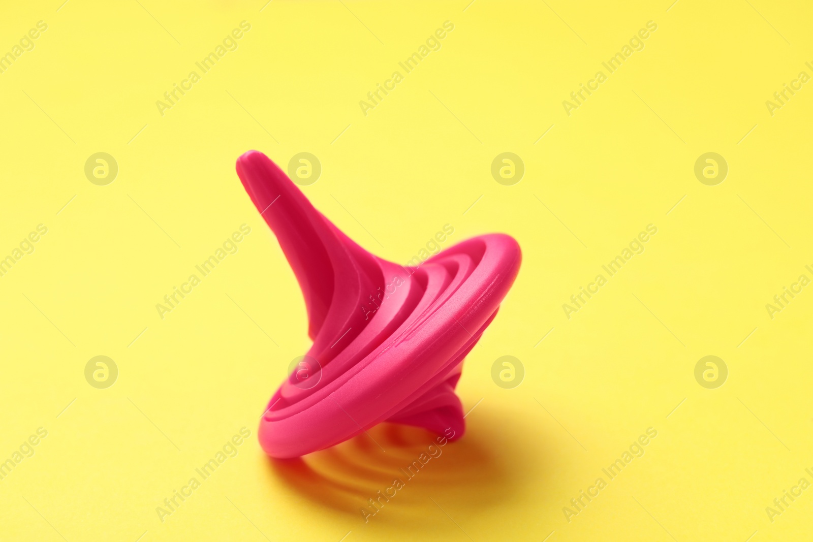 Photo of One pink spinning top on yellow background, closeup