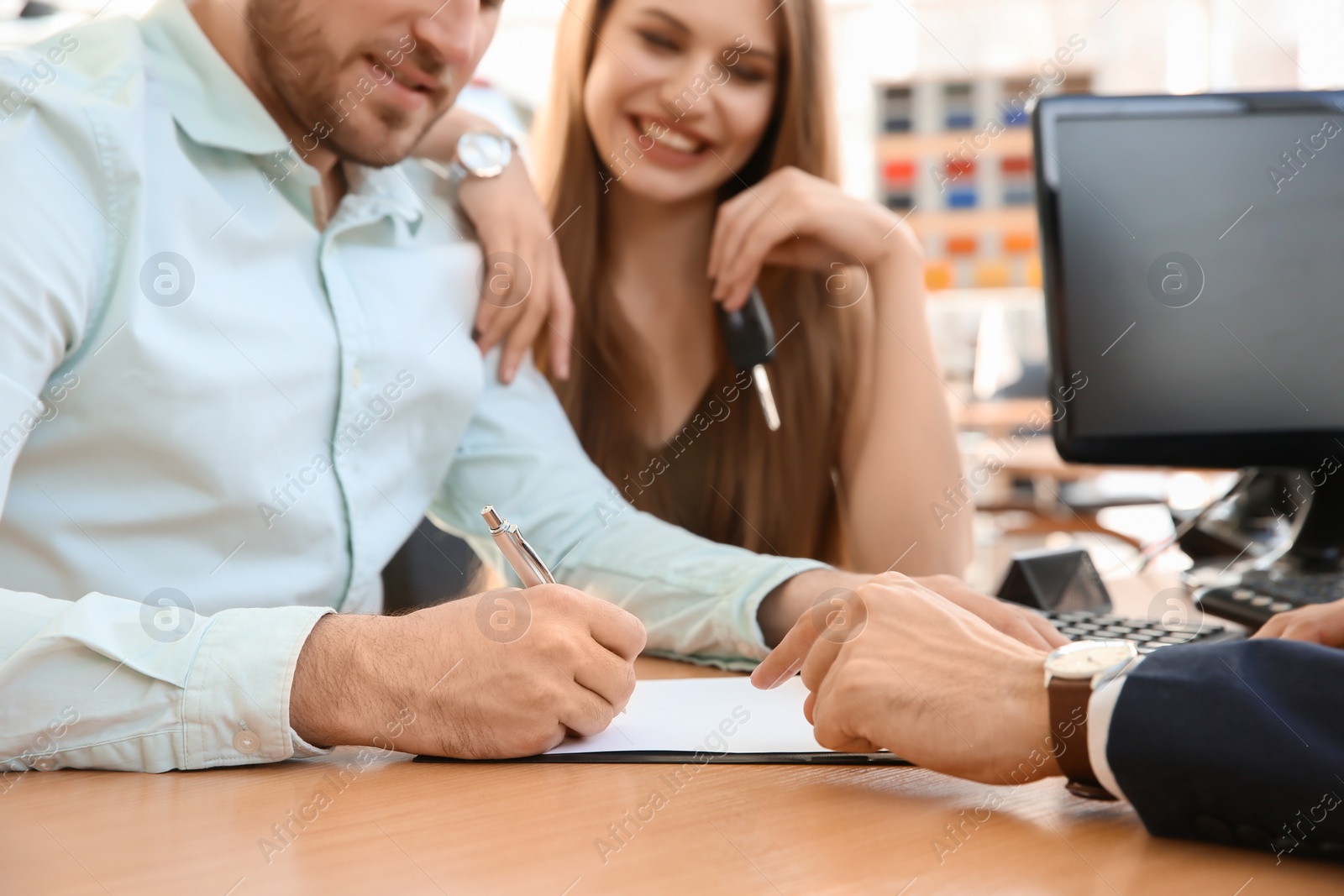 Photo of Young couple and salesman sitting at table in car salon. Buying auto