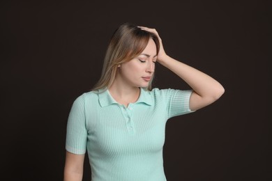 Young woman suffering from headache on dark brown background
