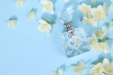 Aromatic perfume in bottle and beautiful jasmine flowers on light blue background, flat lay. Space for text