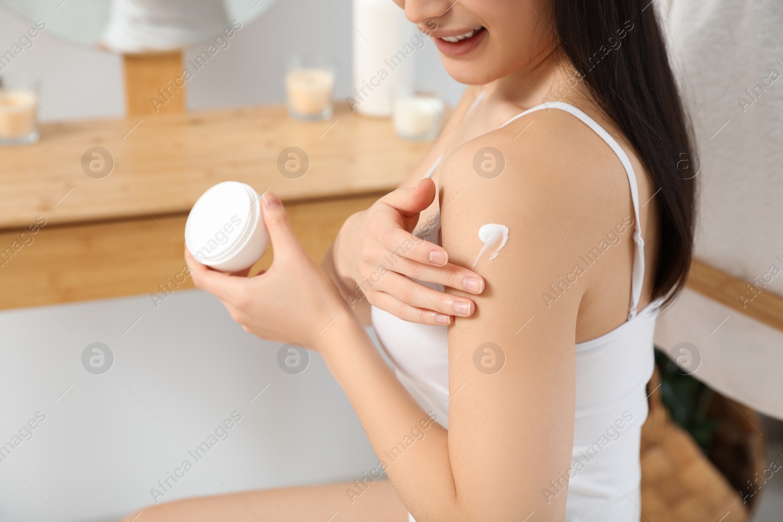 Photo of Young woman applying body cream on shoulder in room, closeup. Space for text