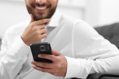 Young man using smartphone indoors, selective focus