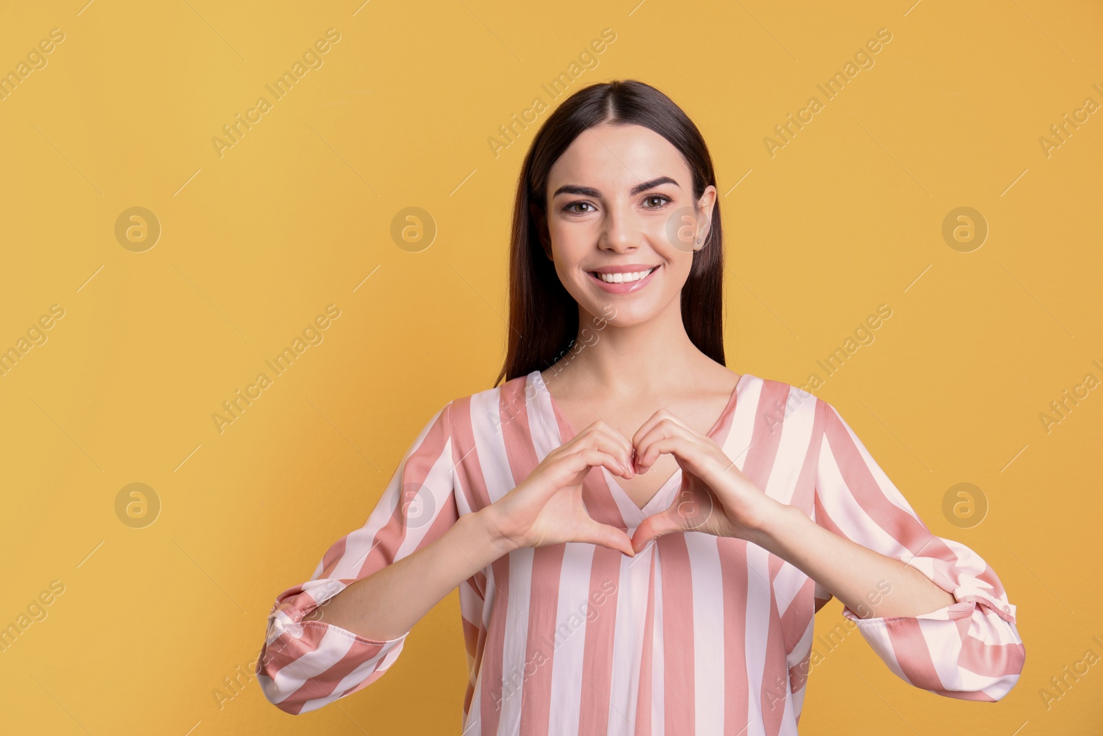 Photo of Portrait of young woman making heart with her hands on color background