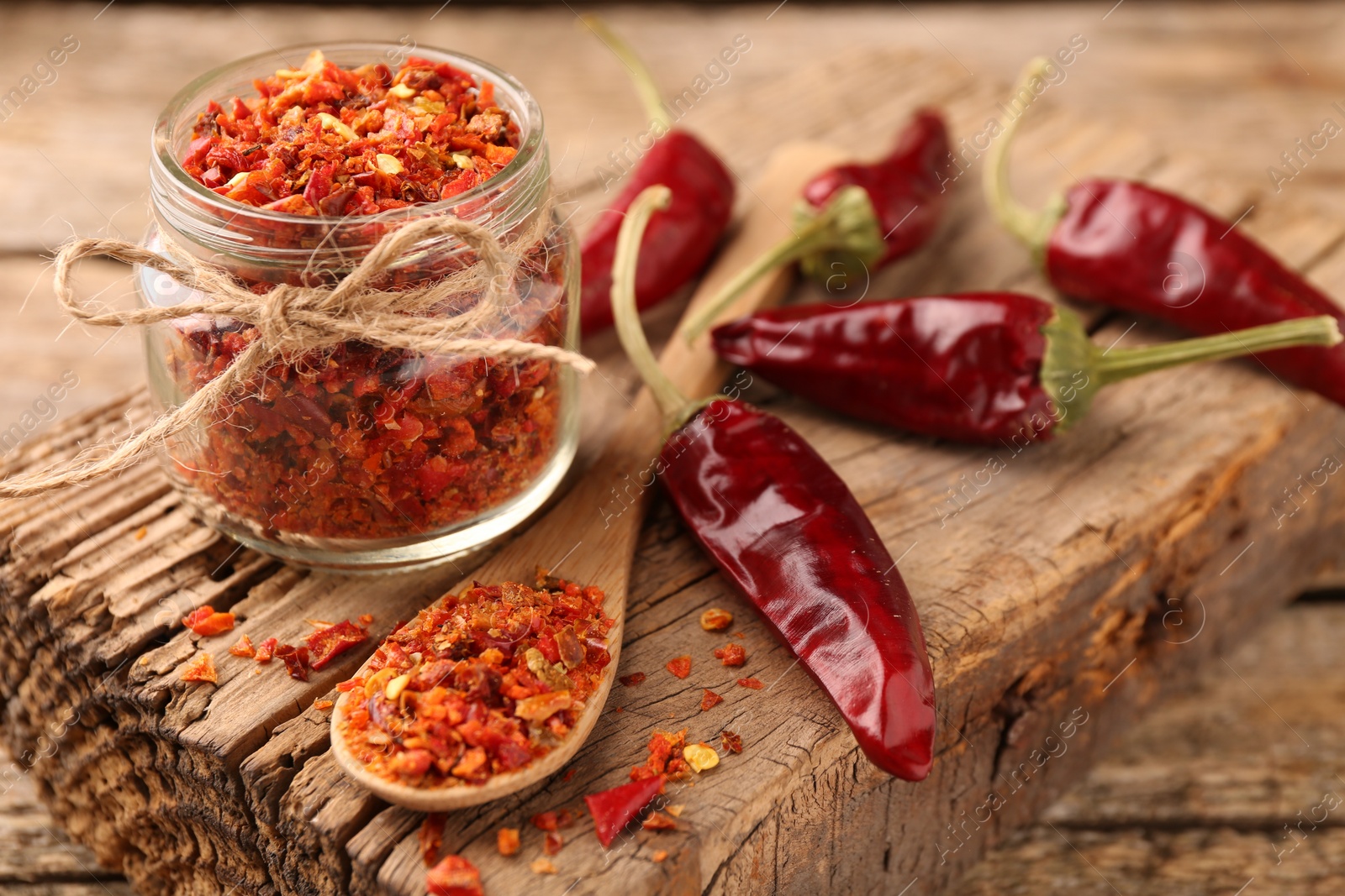 Photo of Chili pepper flakes and pods on wooden table, closeup